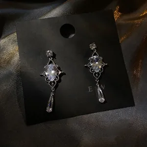 Macro detail of silver-tone teardrop zircon earrings with intricate cutout metal design