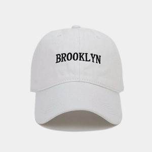 Detail of white cotton baseball cap featuring black Brooklyn embroidered lettering