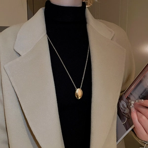Close-up of a minimalist gold oval pendant necklace worn on a black turtleneck sweater