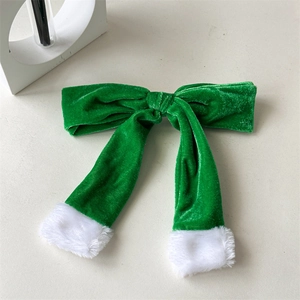 Detailed view of a green velvet Christmas bow hair clip with white plush trim and streamers