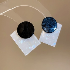Macro shot of square shell and round wood bead earrings on a clear jewelry stand