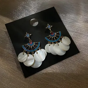 Detail of fan-shaped tassel earrings with blue beads and white shell disks