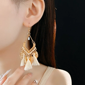Close-up of bohemian gold leaf tassel earrings worn by a model against black background