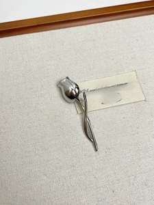Detailed view of silver tulip brooch with mirror polished finish on gray linen background
