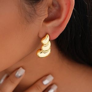 Close-up of golden teardrop earring with organic layered design worn by a model