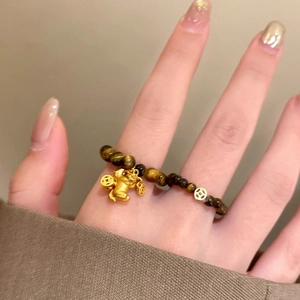 Detail of tiger eye bead ring with golden pig charm and coin bead on model finger
