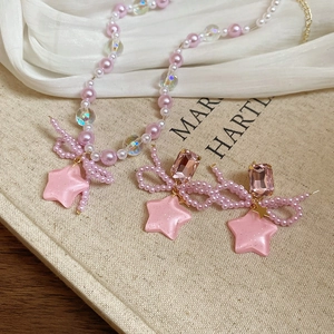 Detail of pink pearl necklace with star pendant and woven bow earrings on soft fabric