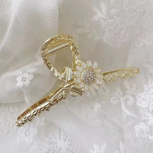 Detail of golden metal hair claw with white flowers and sparkling rhinestones
