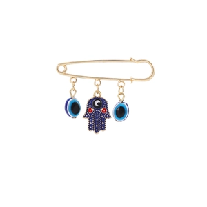 Macro detail of golden Hamsa hand and blue Evil Eye charms on safety pin brooch