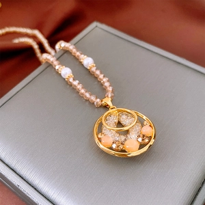Détail du collier avec pendentif doré, perles translucides et perles blanches sur boîte