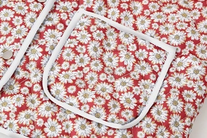 Detail van rode gewatteerde jas met witte madeliefjesprint en zak met knoopsluiting
