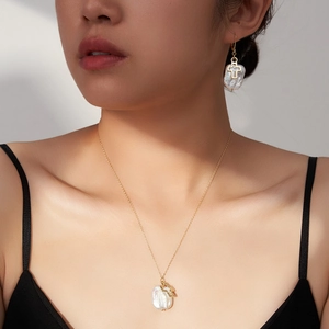 Detailed view of Baroque pearl earrings and cross necklace set on a female model