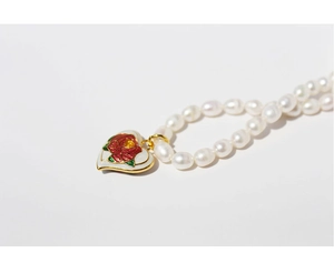 Detail of a gold-plated heart pendant with red rose enamel and white pearls