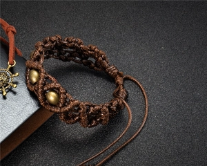 Detailed shot of brown woven bracelet featuring three metal beads and a nautical rudder charm
