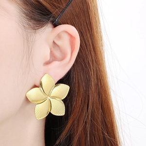 Gros plan sur des boucles d'oreilles pétales dorées à texture radiale portées sur l'oreille