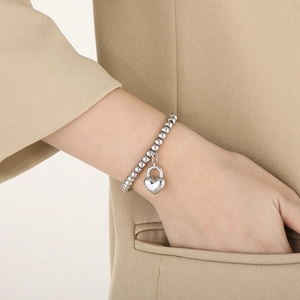 Silver bead bracelet with heart lock pendant shown on model in a beige suit pocket