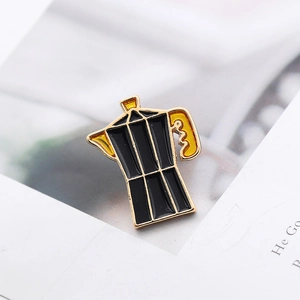 Macro view of a black and gold moka pot enamel pin on a minimalist white background