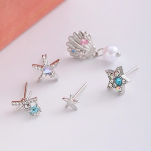 Dettaglio di cinque orecchini in argento con stella marina blu e perle bianche da donna