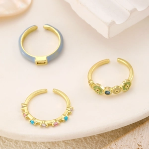 Detail of three adjustable gold-plated rings with blue enamel and colorful gemstones