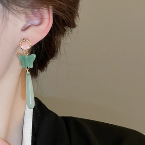 Close-up of elegant butterfly drop earrings with cat-eye resin stone on a model