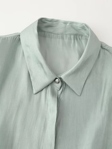 Detail of light green satin shirt collar with silver button and glossy fabric texture