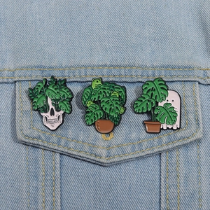 Detailed close-up of three botanical enamel pins with ghosts and skulls on a denim jacket