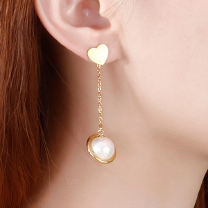 Golden heart stud earrings with a delicate chain and pearl drop pendant on a model