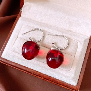 Macro view of C-shaped silver earrings with red apple resin pendants in a jewelry box