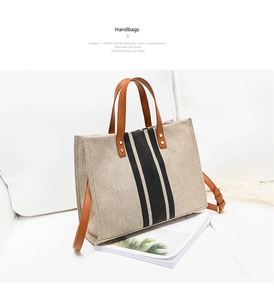 Close-up of beige canvas tote with black stripes and brown leather handles on white background
