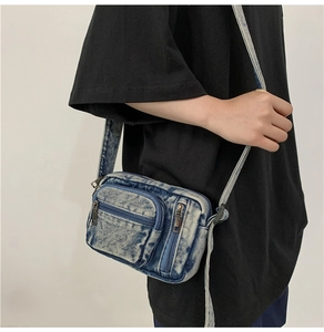 Detailed view of blue denim crossbody bag texture and front zipper pocket detail