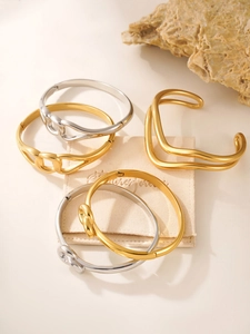 Macro detail of polished gold and silver interlinked bracelets on a beige minimalist background