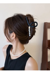 Détail d'une pince à cheveux noire mate avec perles suspendues sur un chignon français