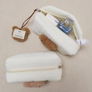 Detail view of quilted cream makeup bag with a cute plush bear charm and soft fuzzy texture