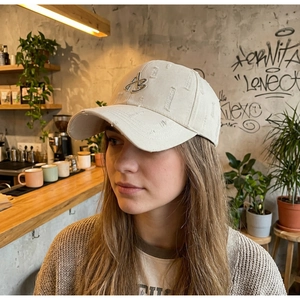 Detail of distressed beige baseball cap with metal AB embroidery and ripped texture