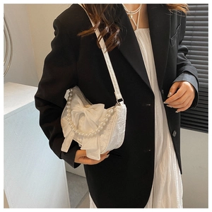 Detail of white bow bag with pearl handle and pleated texture on a model's arm