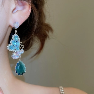 Close-up of elegant butterfly drop earrings with blue and white crystals on a model