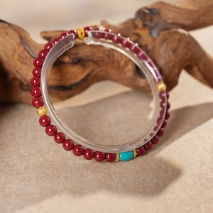 Detail of red cinnabar beaded bracelet with gold hollow beads and turquoise charm