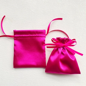 Detail of two glossy rose red satin drawstring gift bags on a white textured surface