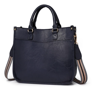 Sac fourre-tout bleu foncé en cuir avec bandoulière rayée et coutures élégantes sur fond blanc