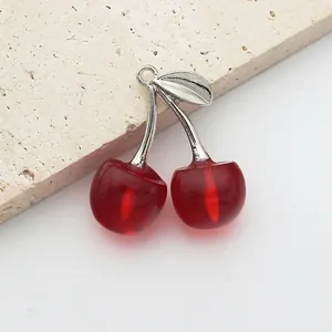 Detailed view of DIY red crystal cherry charms with silver leaves on a textured stone surface