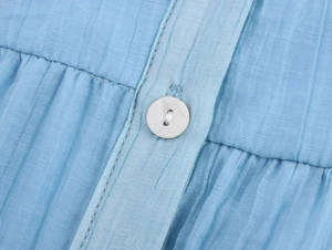 Detail of light blue pleated fabric with high-quality white round button and fine stitching