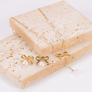 Elegant gold bow necklace and pearl earrings set displayed on decorative stone