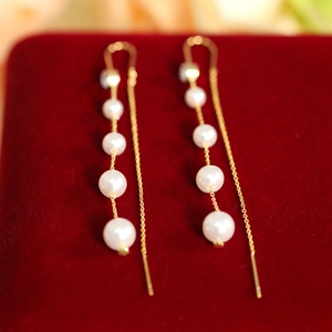 Detail of elegant gold tassel earrings with cascading white pearls on red velvet