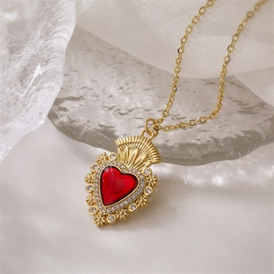 Dettaglio della collana d'oro con ciondolo a cuore rosso e diamanti su stoffa bianca