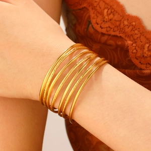 Detail of stacked gold bangles with textured finish on wrist against brown lace