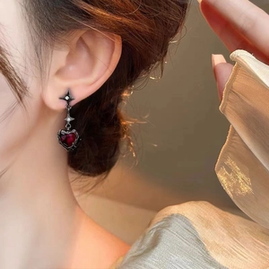 Close-up of a gothic heart earring with dark red gemstone worn by a model