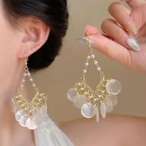 Détail de boucles d'oreilles bohèmes avec fil d'or tissé, perles et disques de nacre