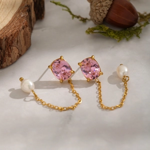 Detailed close-up of gold tassel earrings with pink zircons and white pearls on marble