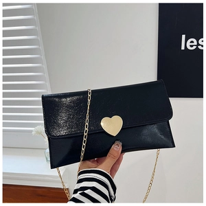 Detail of glossy black patent leather clutch featuring a gold heart buckle and chain strap