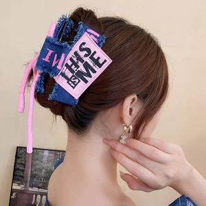 Detail of blue denim hair claw with pink fringe and embroidered text on model hair